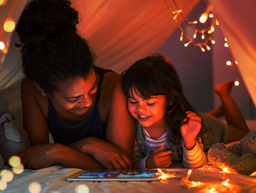 a mother and daughter in a pillow fort looking at a tablet