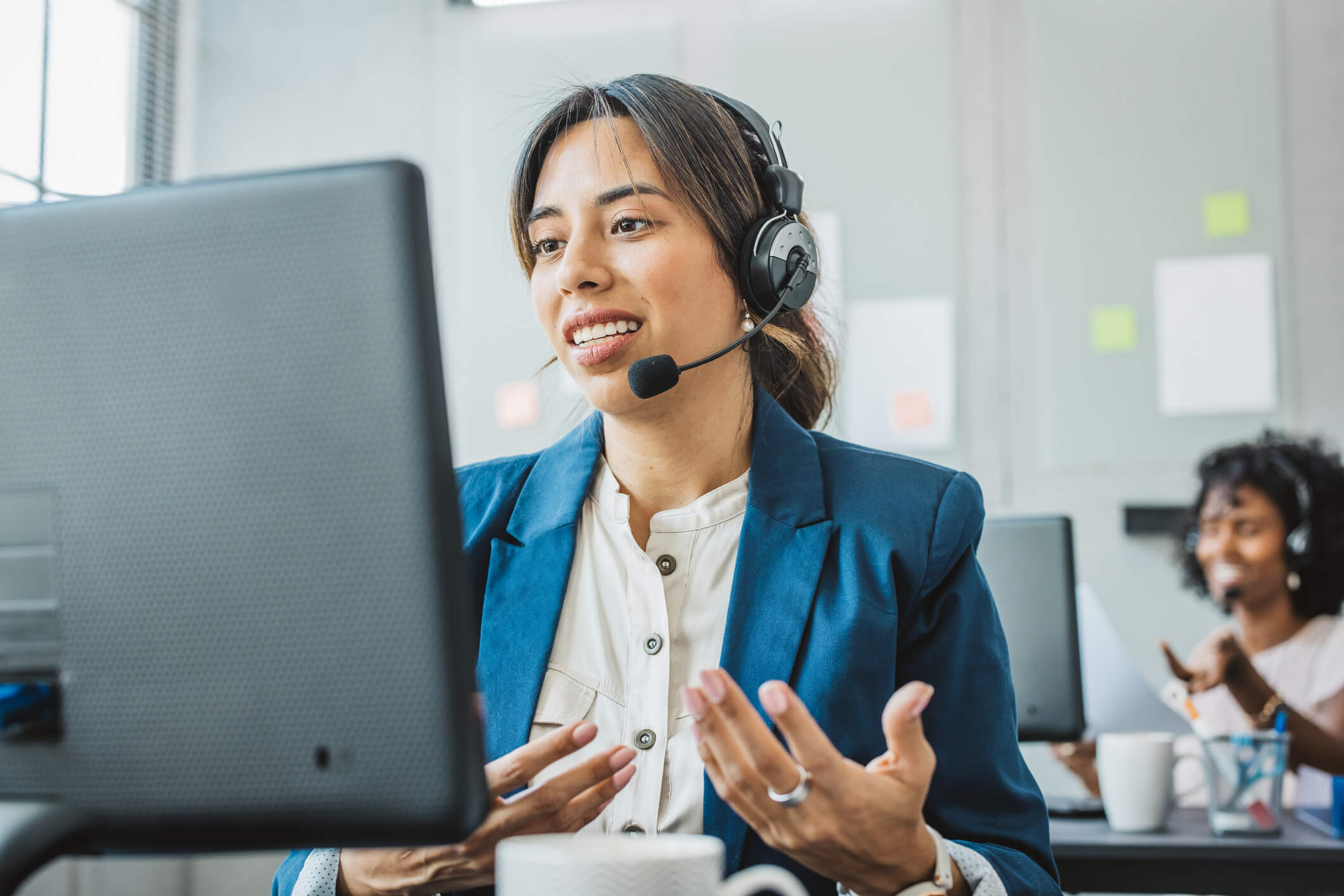 a woman wearing a headset talking to a laptop screen to offer customer support