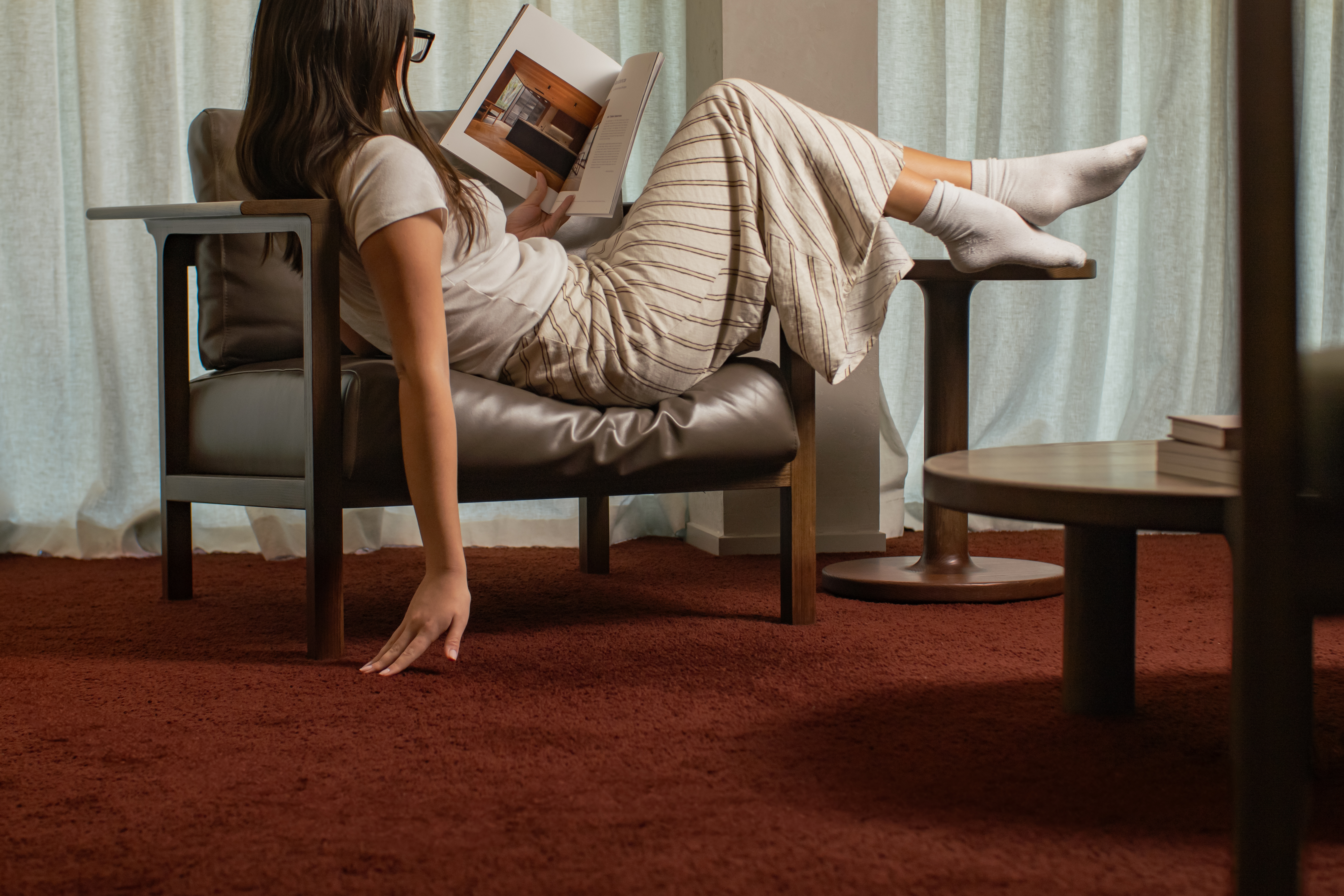 a woman in a chair reading a book, feeling a carpet with her free hand