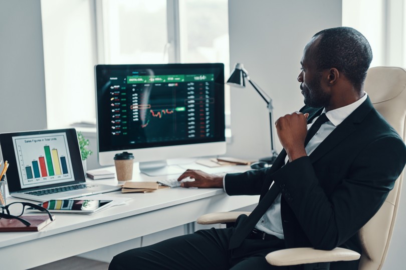 a man in a suit looks at two monitors displaying graphs of data